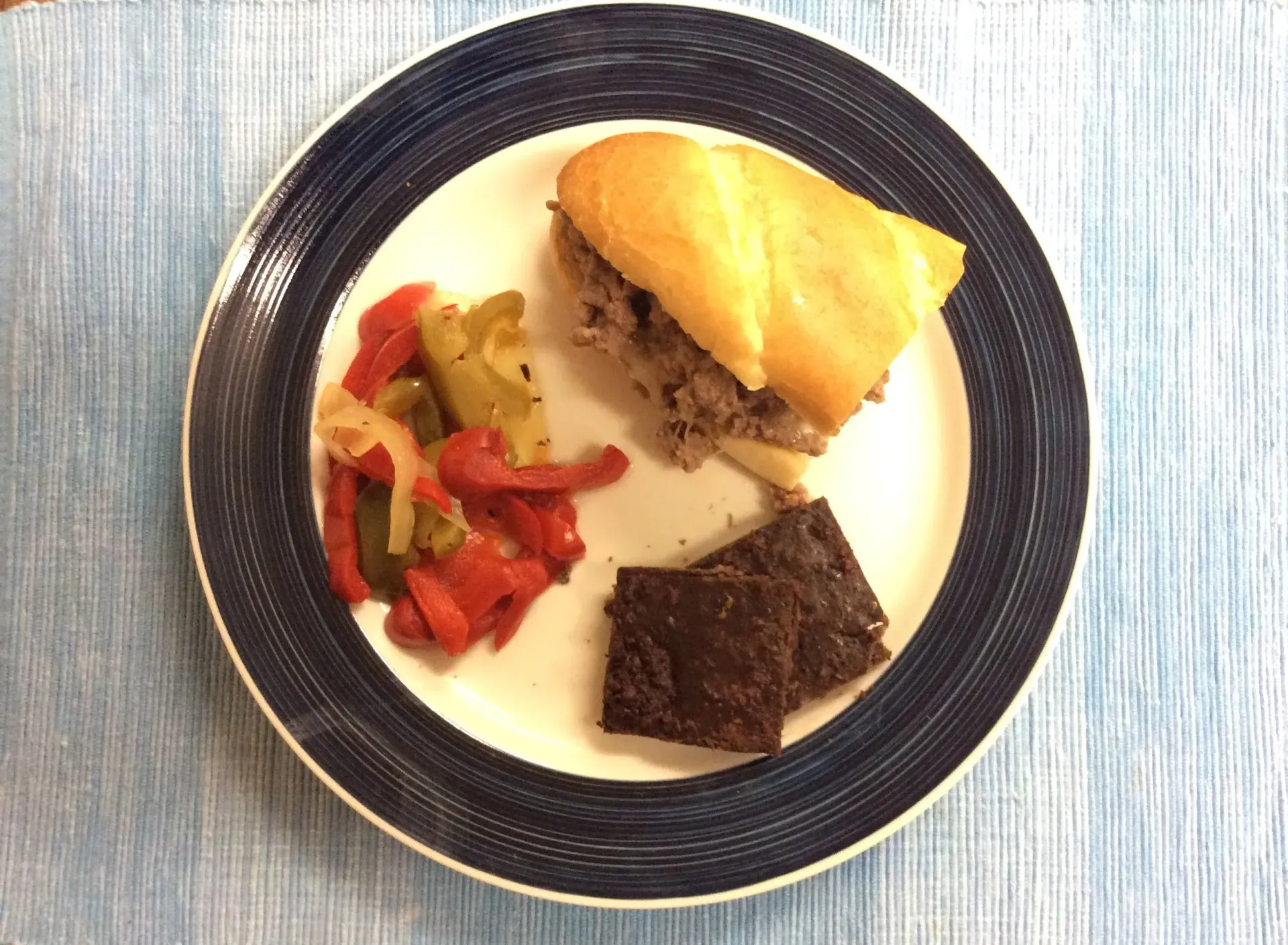 A plate with a sandwich, roasted vegetables, and a piece of chocolate dessert on a white table.