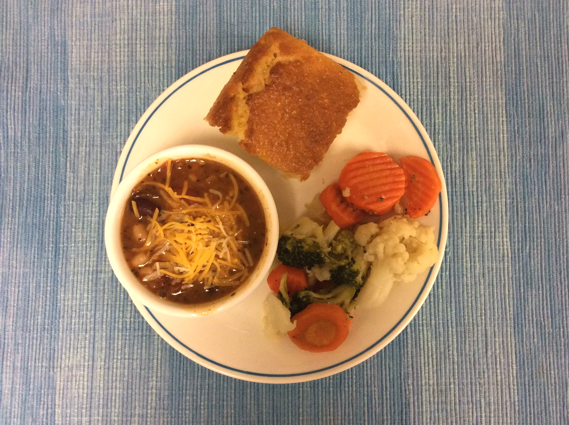Plate with soup, toasted bread, carrots, broccoli, mashed potatoes, and cheese on a blue tablecloth.