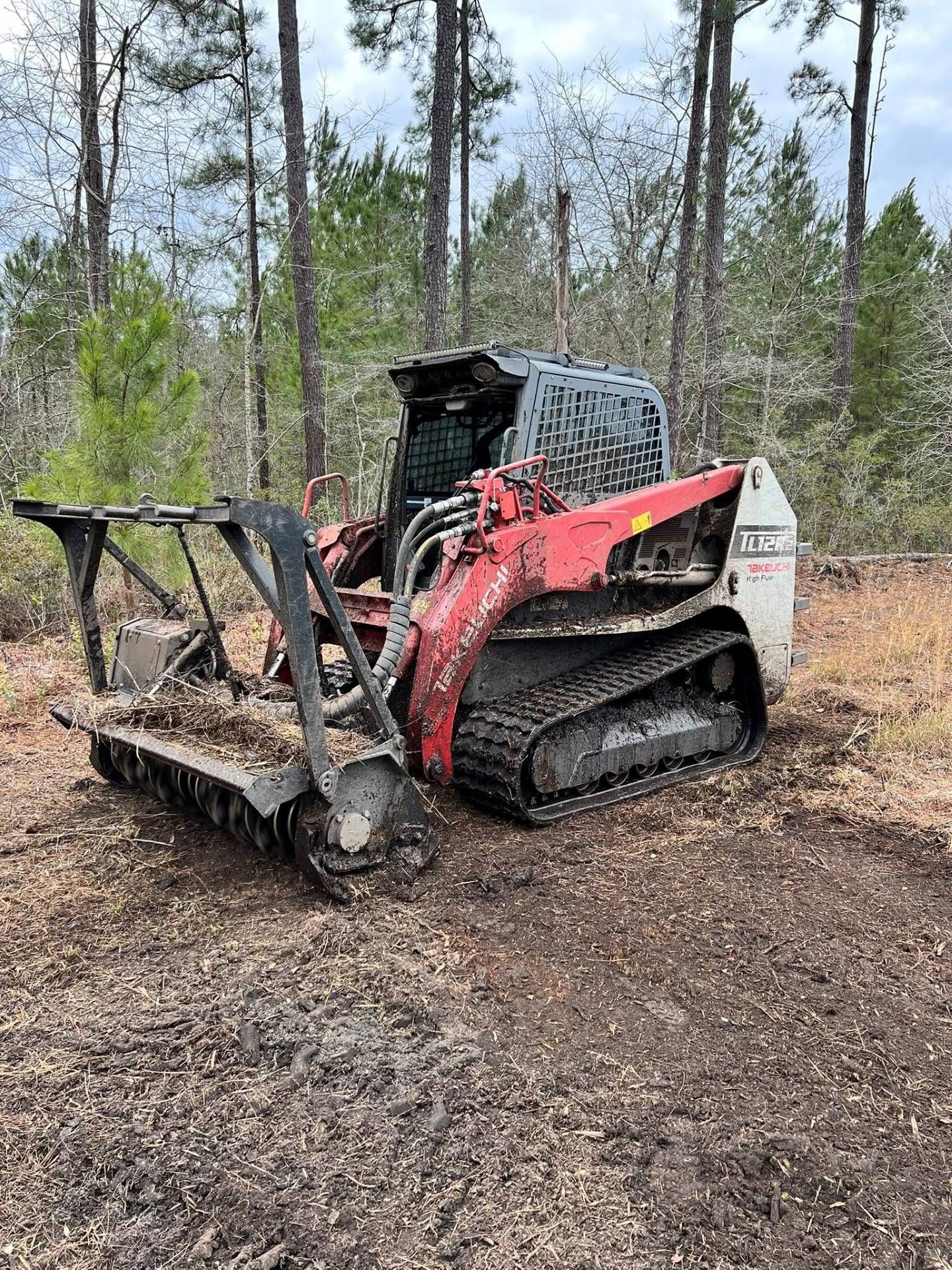Red tracked skid steer with tree-cutting attachment in a wooded clearing