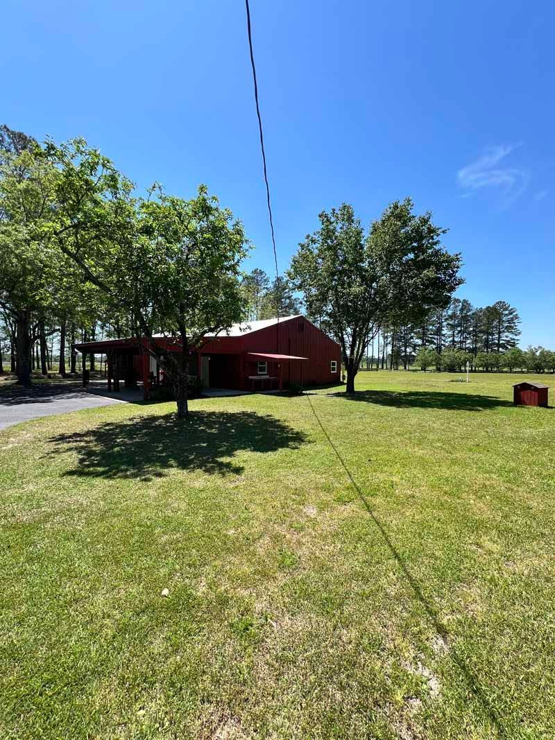 Red building with trees and a grassy field under a bright blue sky