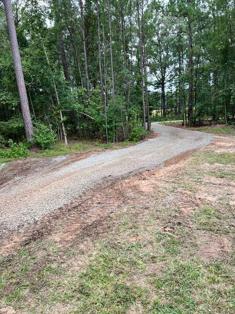 Gravel path curving through a wooded area with green trees and grass