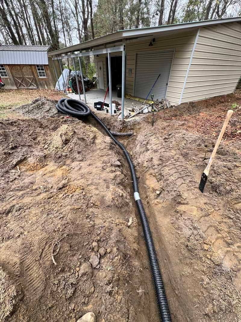 Backyard construction with a trench, black hose, and a shed beside a muddy slope