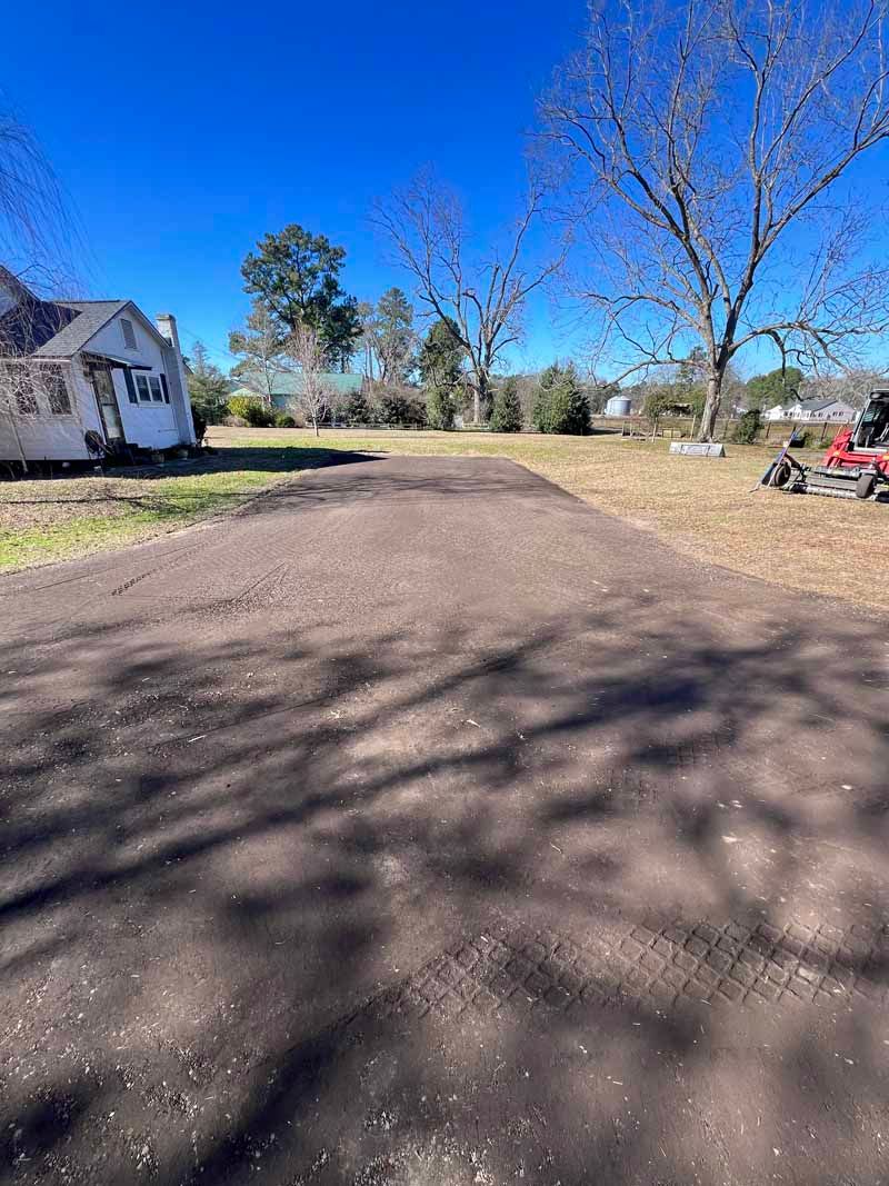 Wide dirt driveway beside a white house with bare trees, blue sky, and a red ATV on the right.