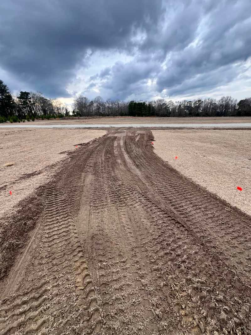 Mud tire tracks across a flat dirt field under dark, cloudy sky.