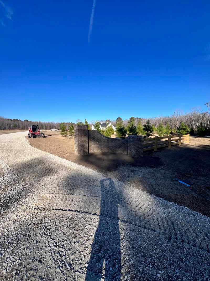 Gravel path with a black fence and trees under a bright blue sky