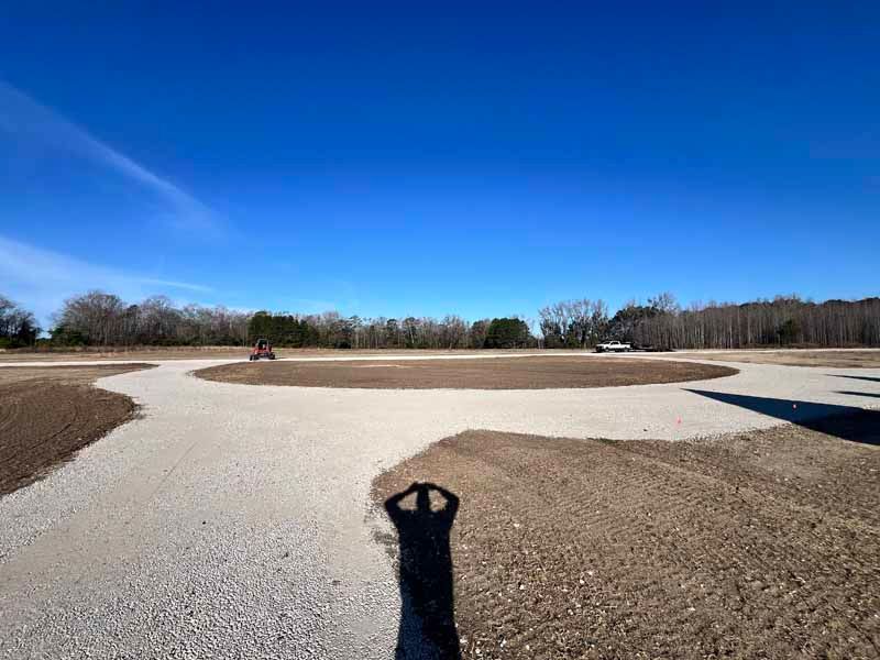 Golf course green with sand bunkers under a bright blue sky, shadow of a person in the foreground