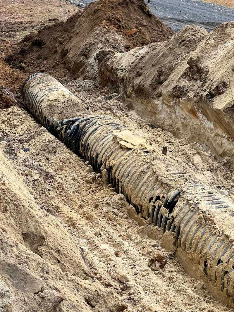 Large buried pipeline exposed in a muddy trench at a construction site