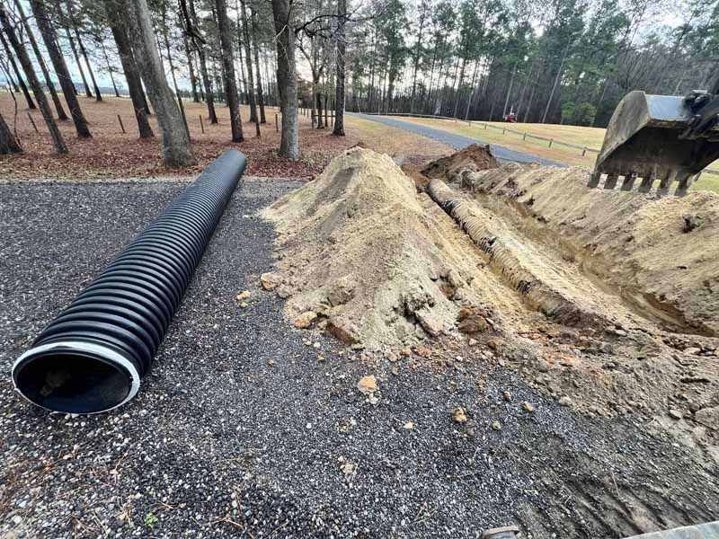 Black drainage pipe beside a dirt trench and gravel roadside under construction in a wooded area