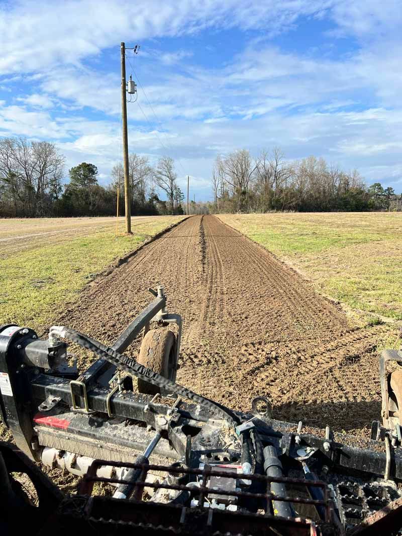 Tractor view of a freshly tilled dirt field with power poles and trees under a blue sky