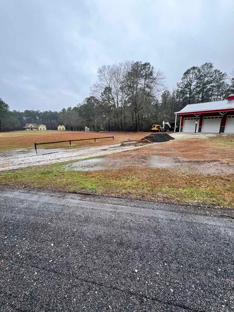 Rainy gravel driveway beside a red-roofed building and open field under a cloudy sky