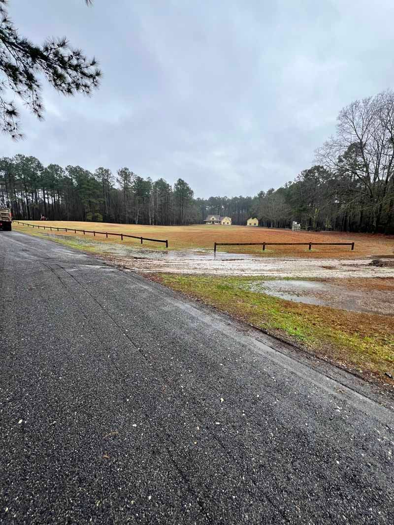 Gravel road beside a flooded field with a tree line under an overcast sky