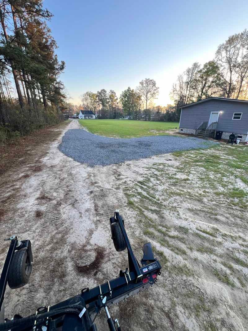 Low-angle view from a bicycle on a gravel driveway beside a grassy yard and house at sunset