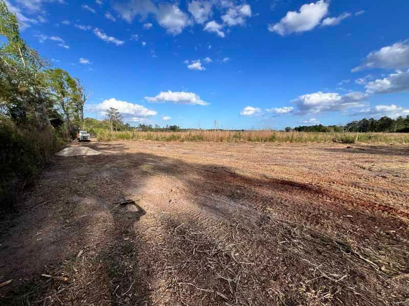 Dry dirt path beside a field under a bright blue sky with scattered clouds