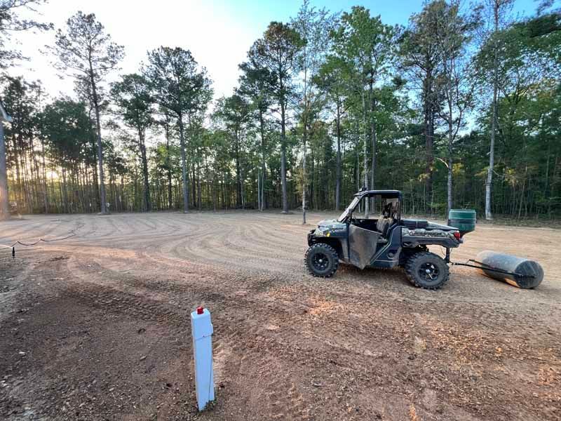 ATV parked on a dirt lot with a water tank, trees lining the background at sunset.