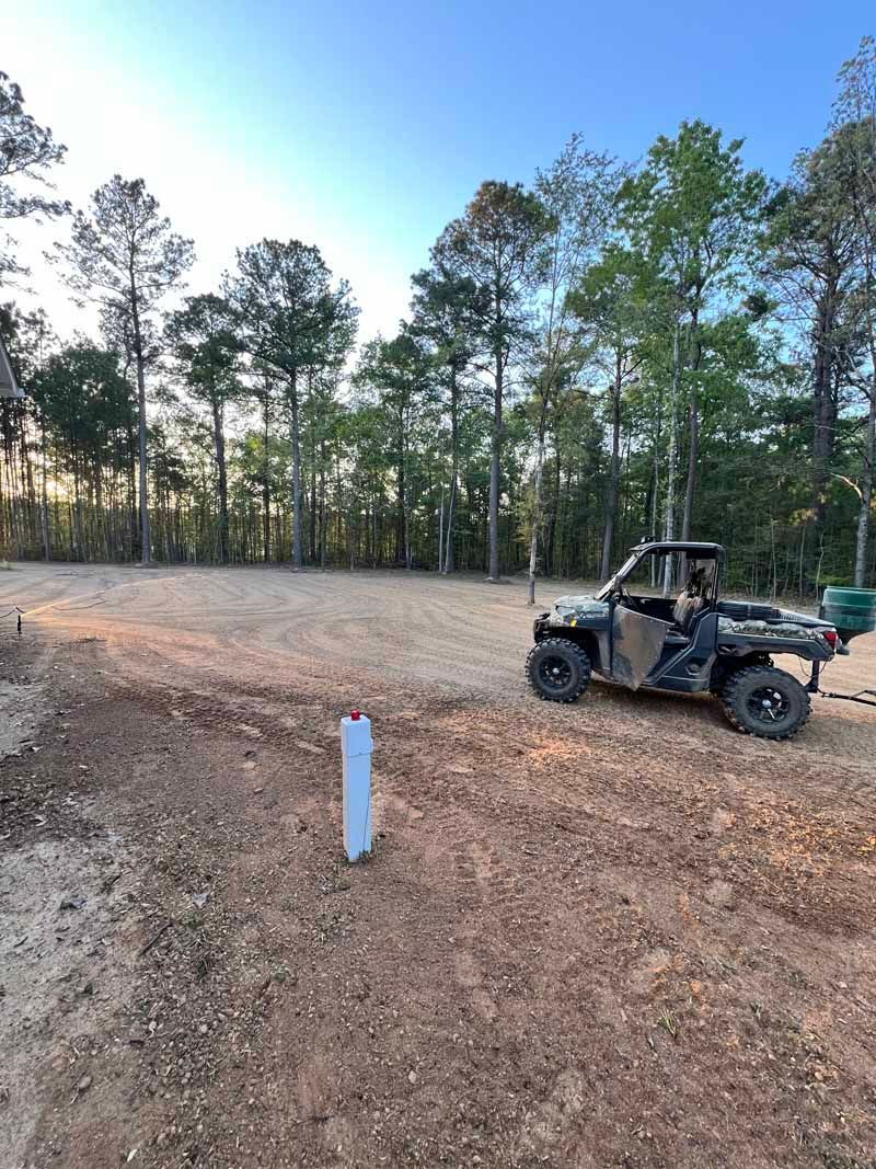 Off-road vehicle parked on a dirt clearing beside trees at sunset