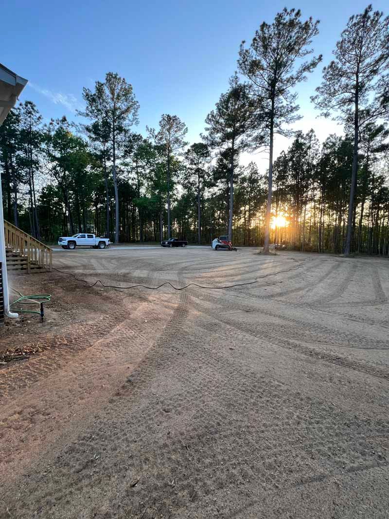 Dirt lot with parked white trucks and tall pine trees at sunset