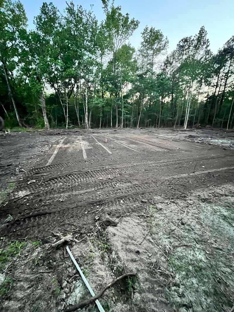 Cleared dirt lot beside a line of green trees at dusk, with a shovel in the foreground.