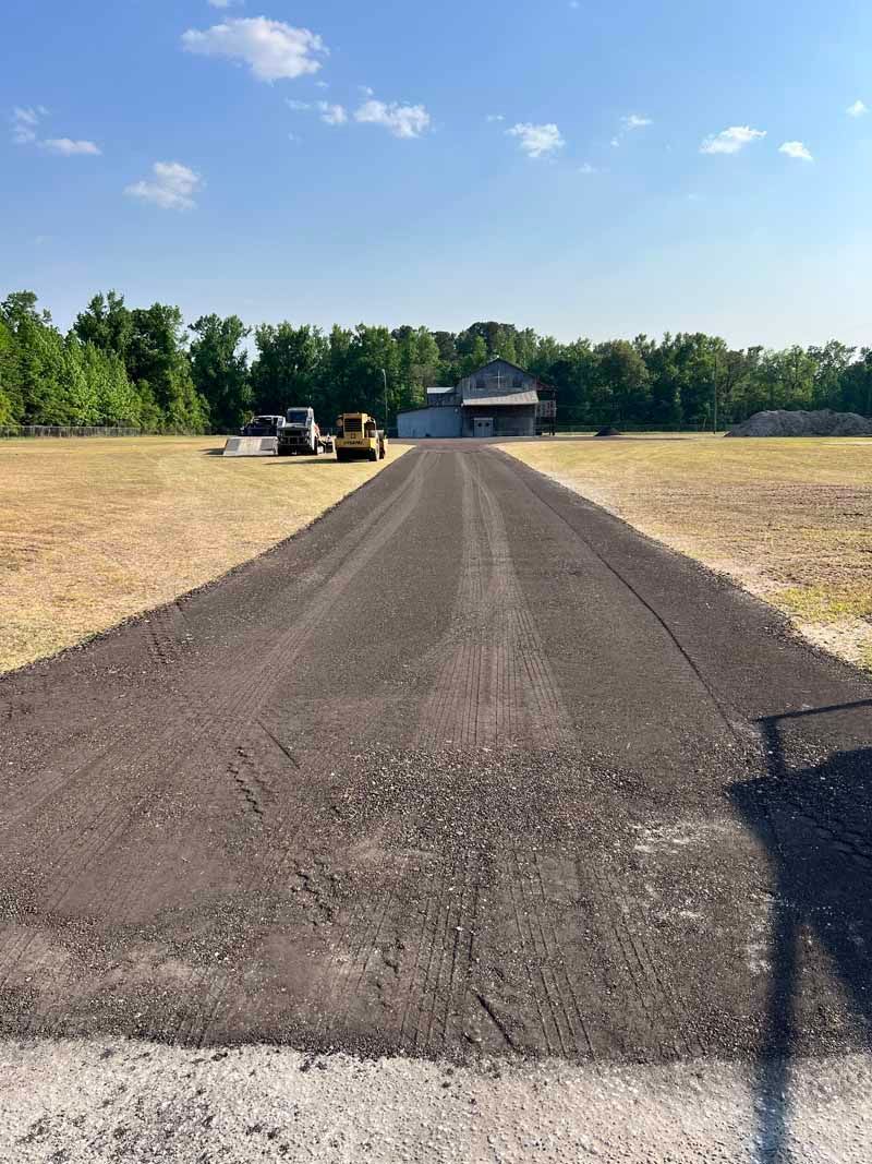 Gravel driveway leading to a house, with two parked vehicles and trees under a blue sky.