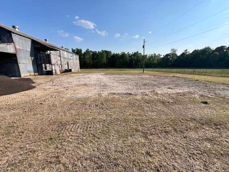 Rustic barn beside a gravel lot under a clear blue sky, with trees in the background