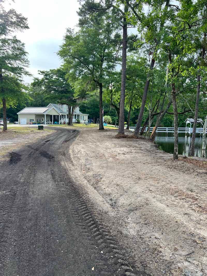 New gravel path beside a wooded lakeshore, with a small house in the background