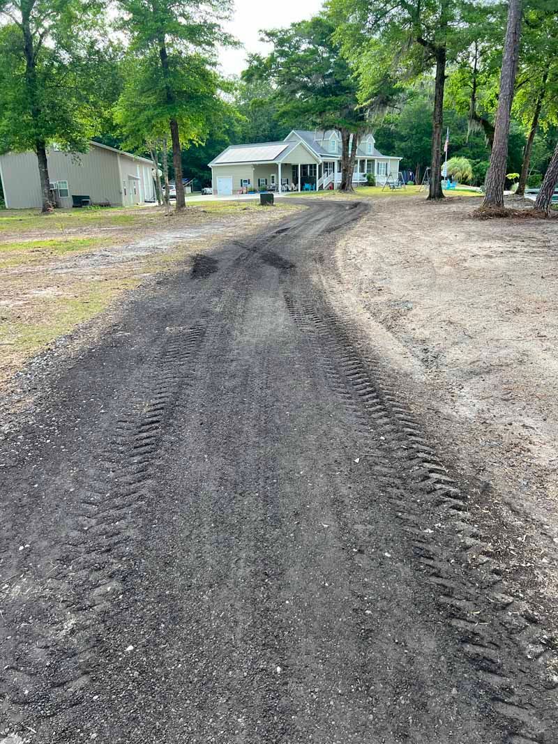 Gravel driveway leading to a white house and trees in a wooded yard