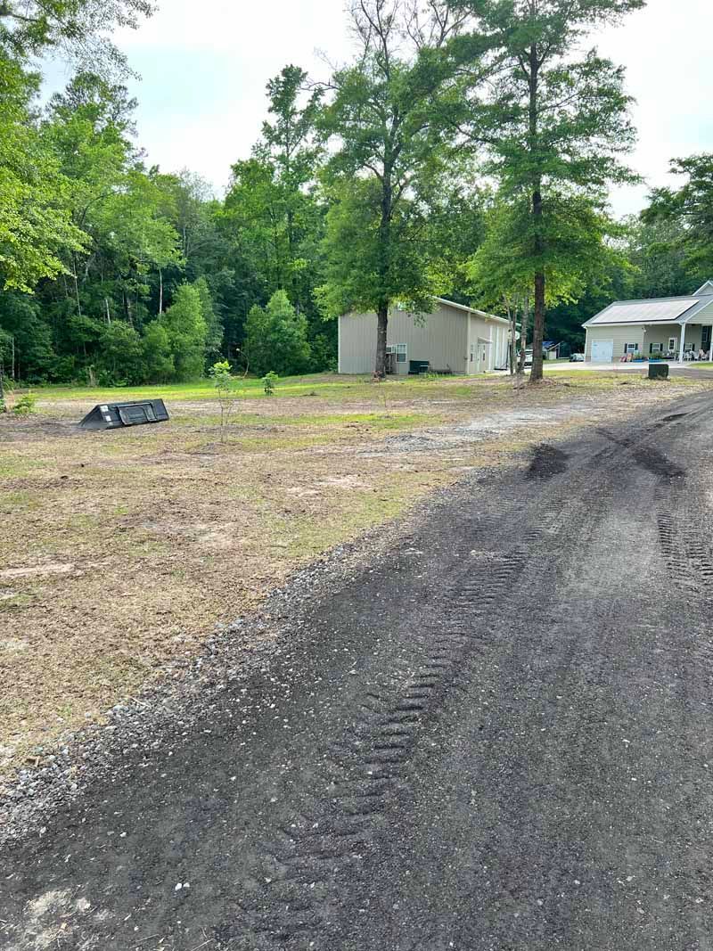 Gravel driveway leading to small white buildings amid trees and open dirt lot