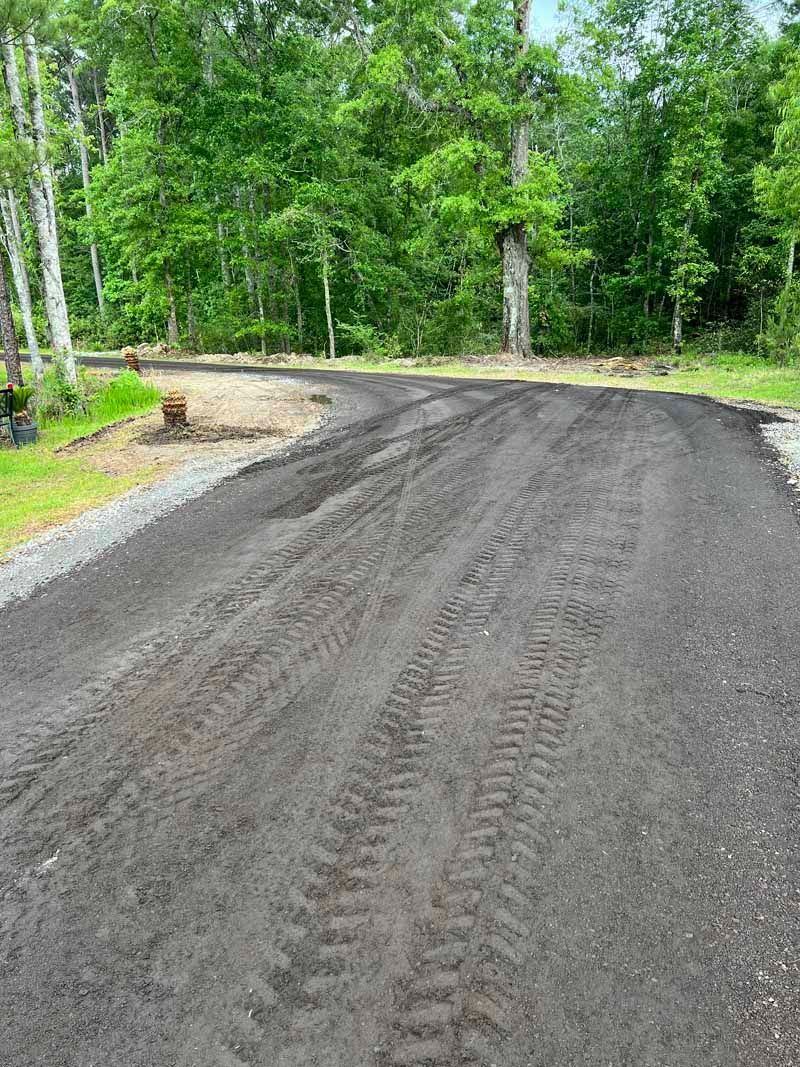 Freshly graded gravel road curving through a green wooded area