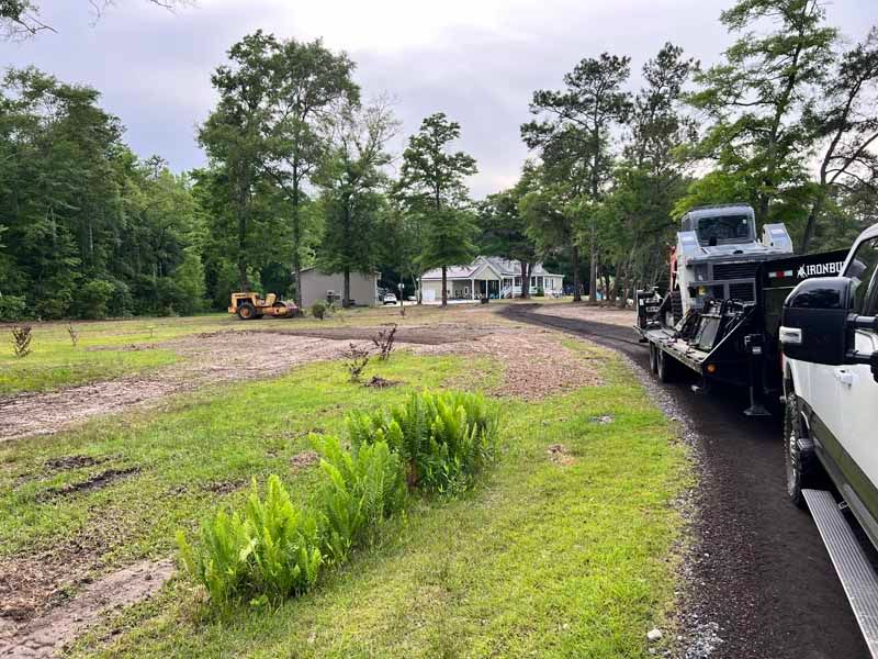 Rural roadside worksite with trucks, excavator, and muddy cleared ground near trees