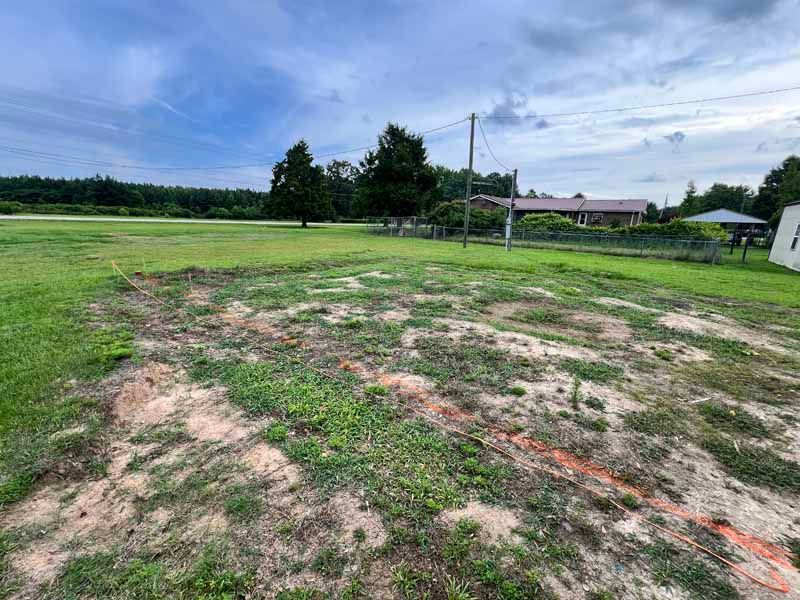 Open grassy field with patches of bare dirt and a volleyball net under a cloudy sky