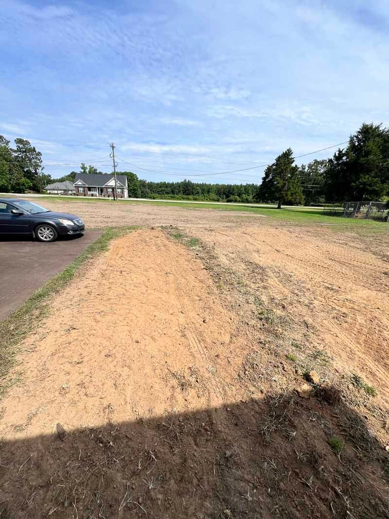Dirt path through a grassy field beside a parked black car under a blue sky