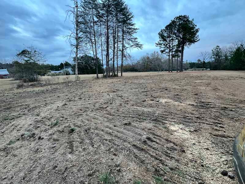Bare, plowed field with tire tracks under a cloudy sky and a few trees in the distance