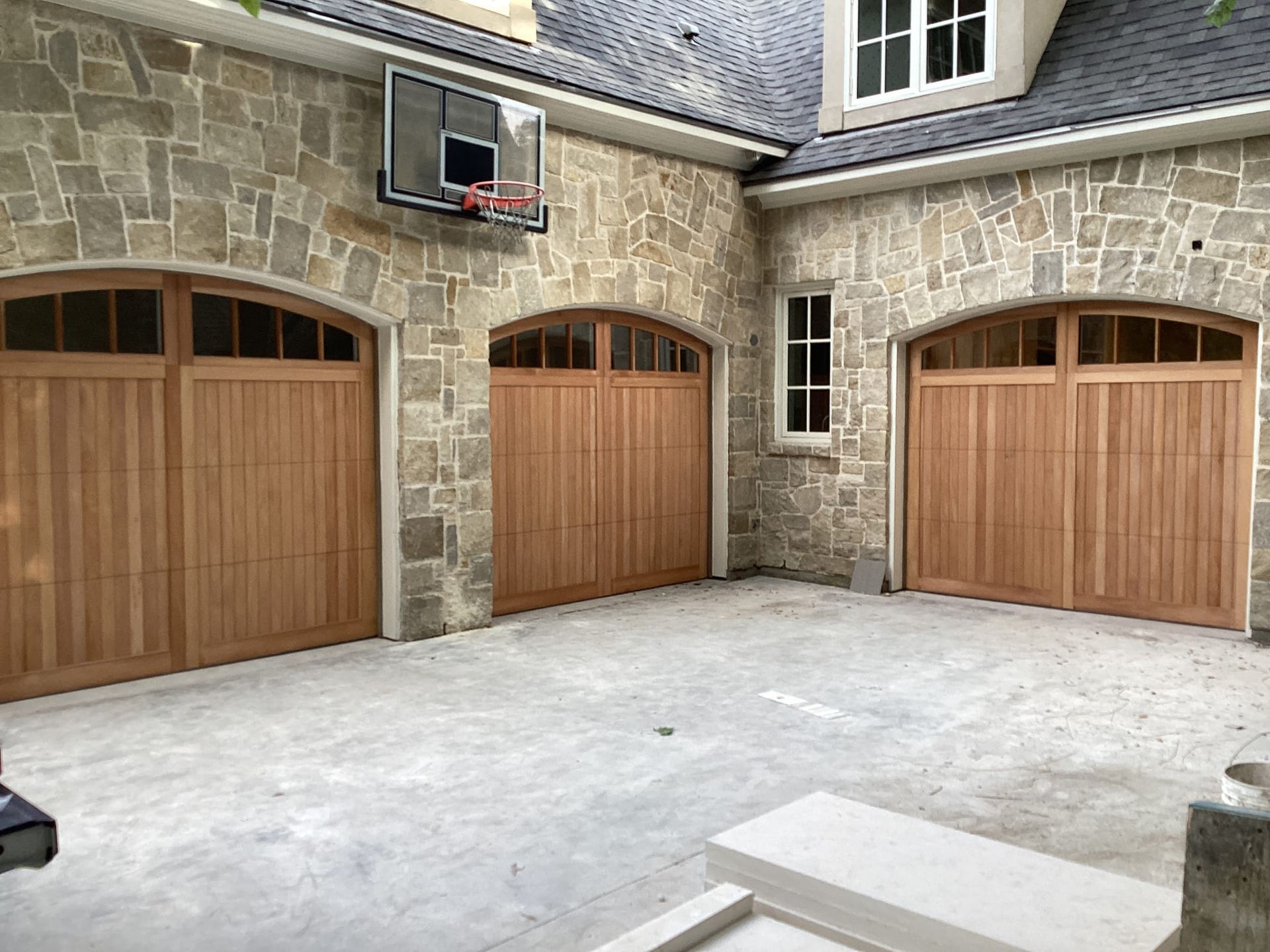 A stone building with wooden garage doors and a basketball hoop hanging from the roof.