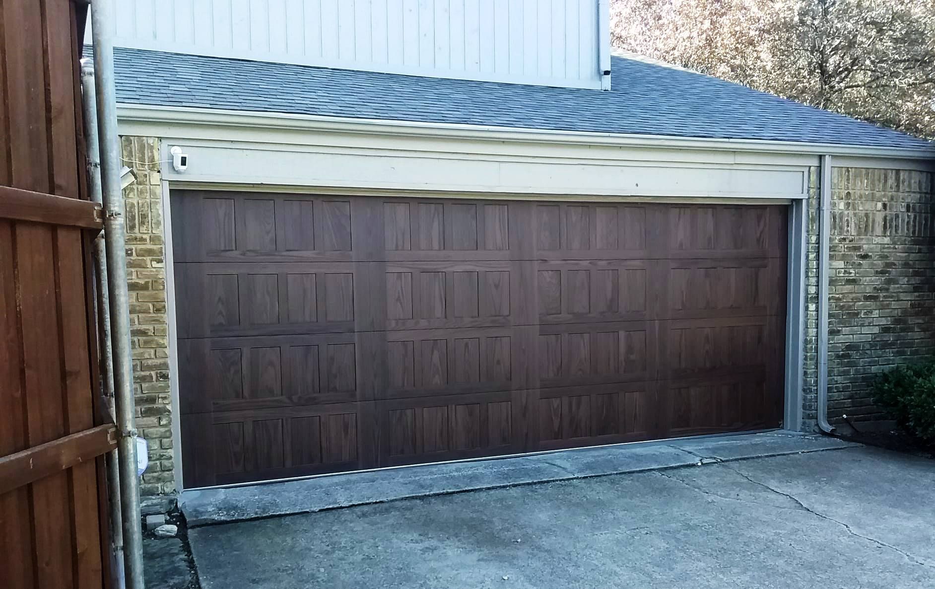 A brown garage door is sitting next to a wooden fence.