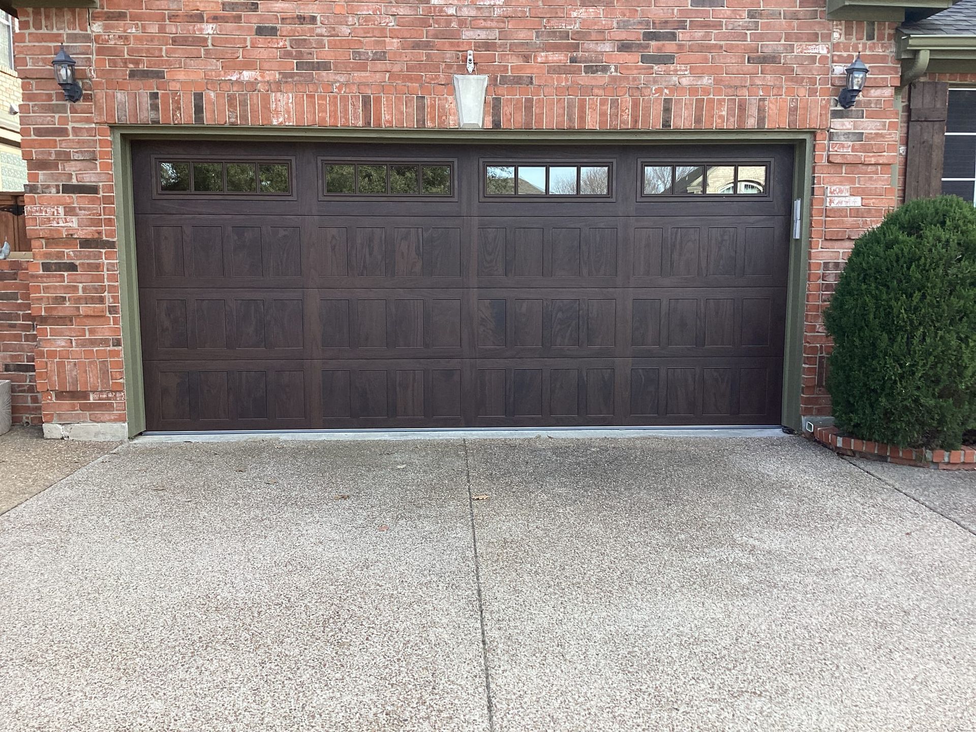 A brown garage door is sitting in front of a brick house.