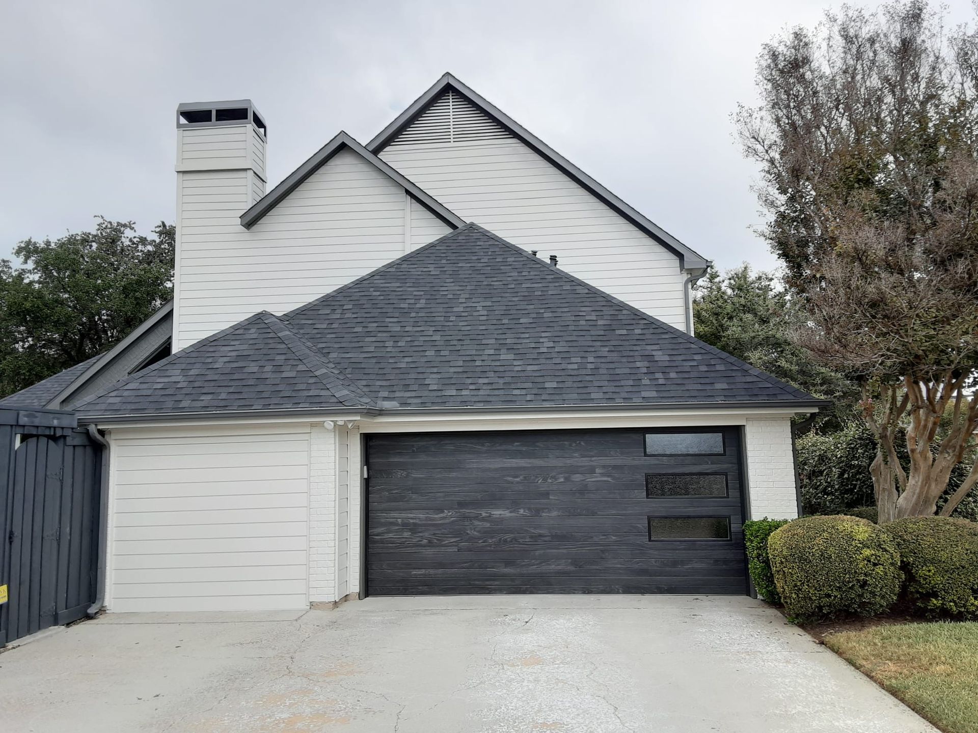 A white house with a black garage door and a chimney.
