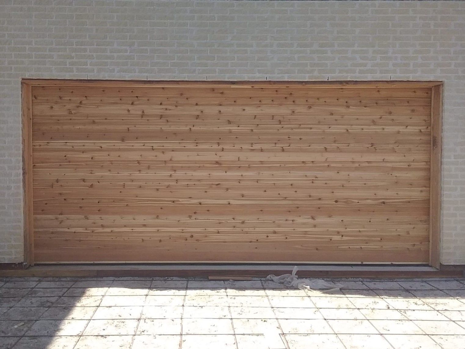 A wooden garage door is against a white brick wall