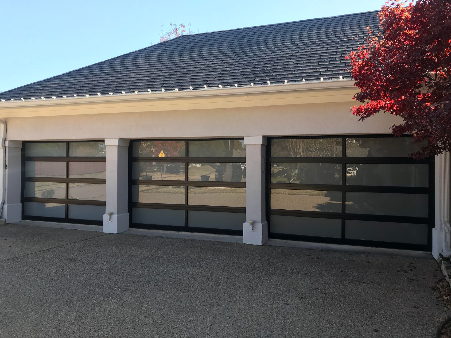 A white house with black garage doors and a tree in front of it.