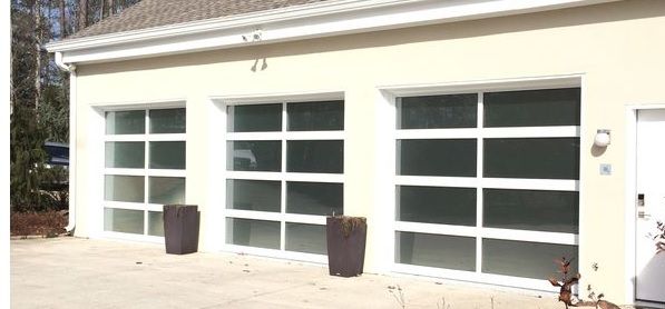 A white house with three garage doors and two potted plants in front of it.