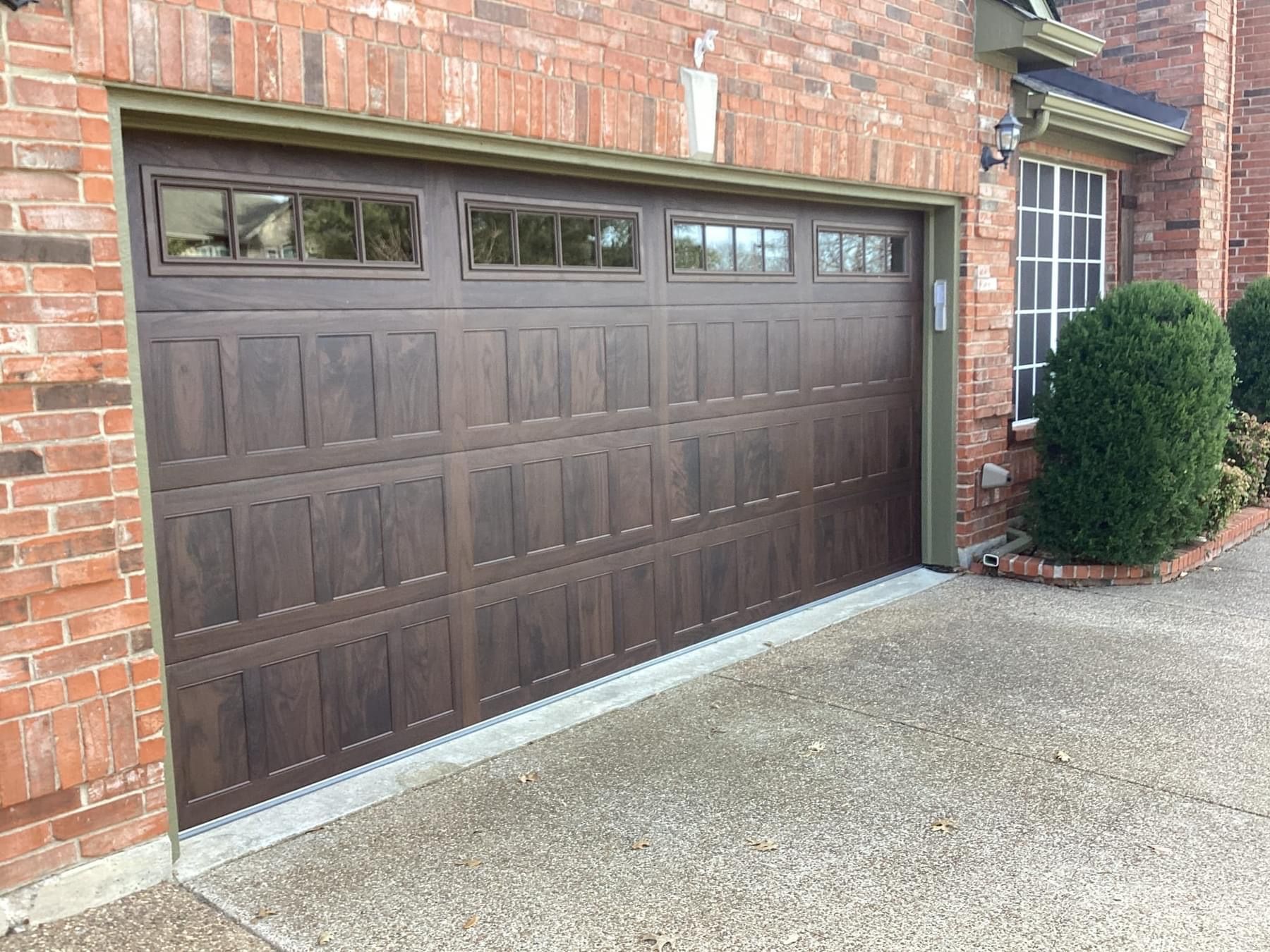 A brown garage door is sitting in front of a brick house.