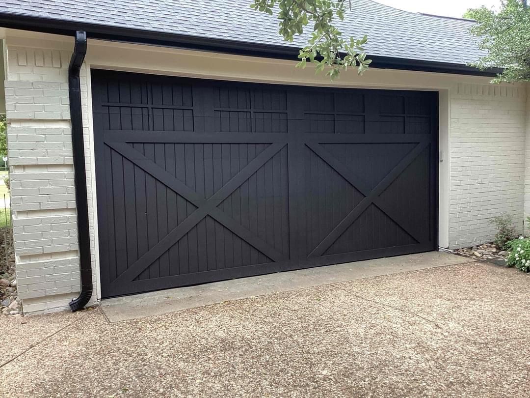 A black garage door is sitting in front of a white house.