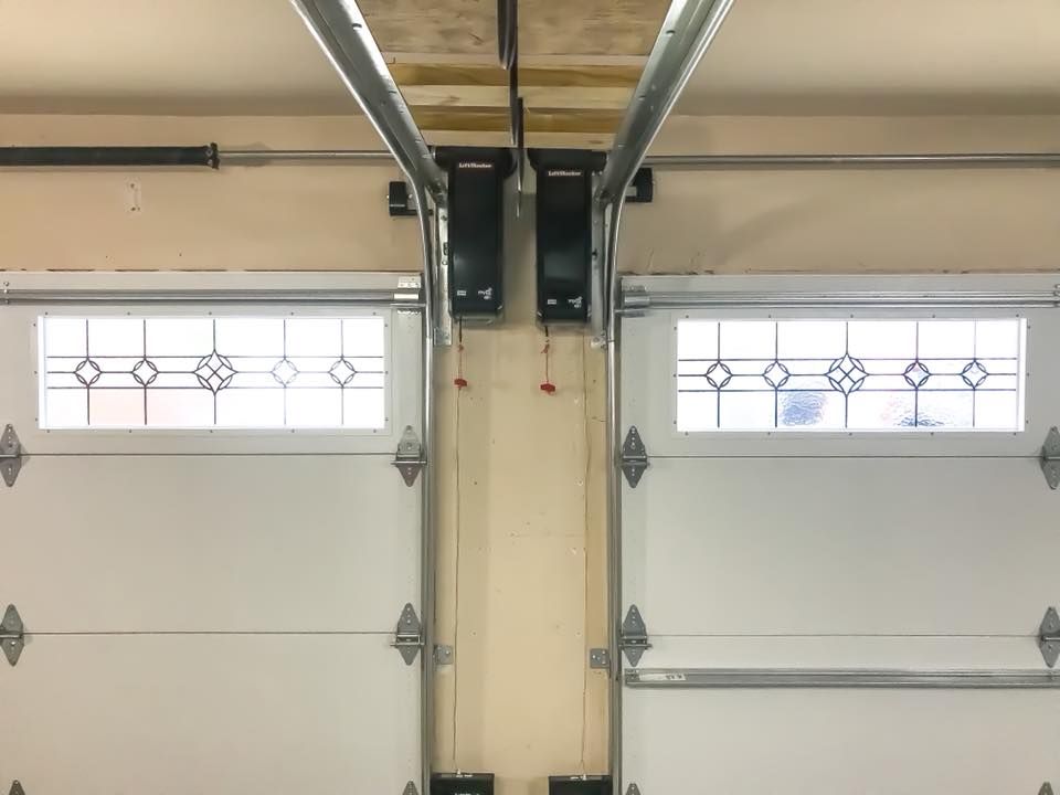Two white garage doors with glass panels, side-by-side, partially open. Rails and support beams overhead.