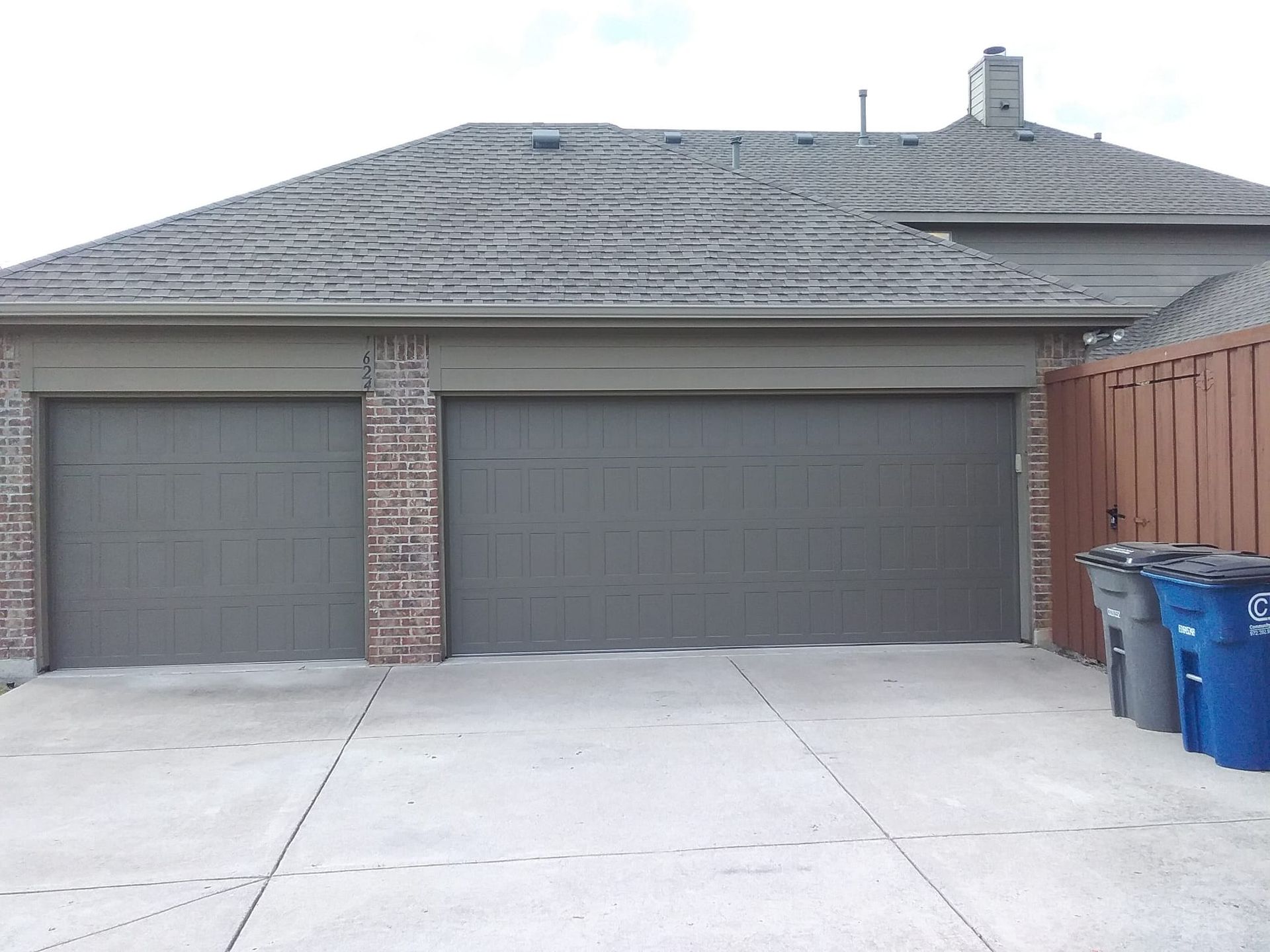 A house with three garage doors and trash cans in front of it