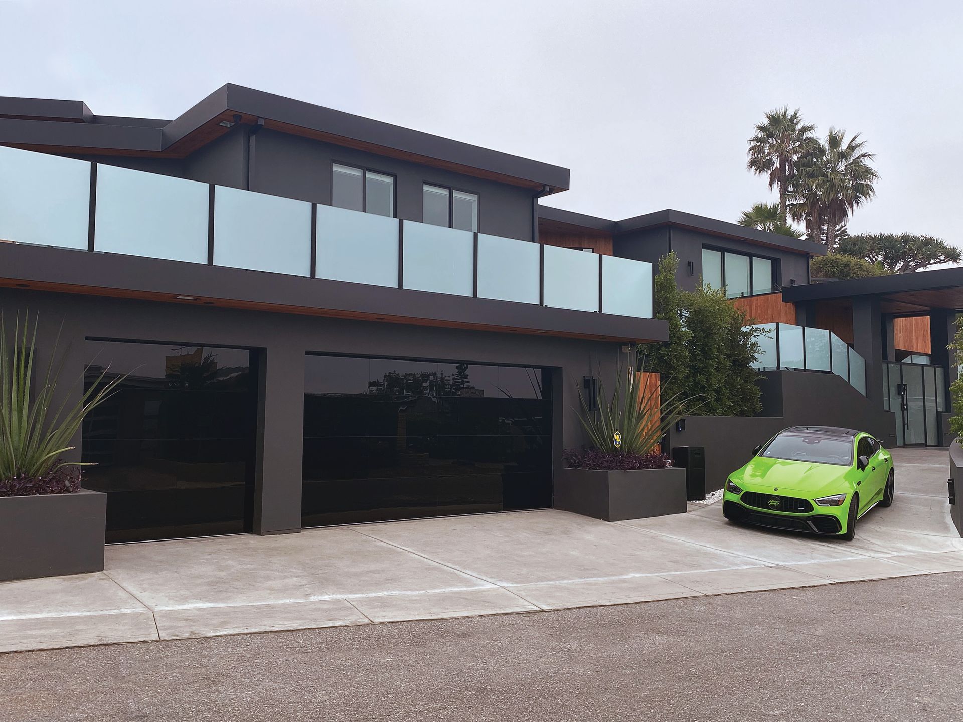 A green car is parked in front of a large house.