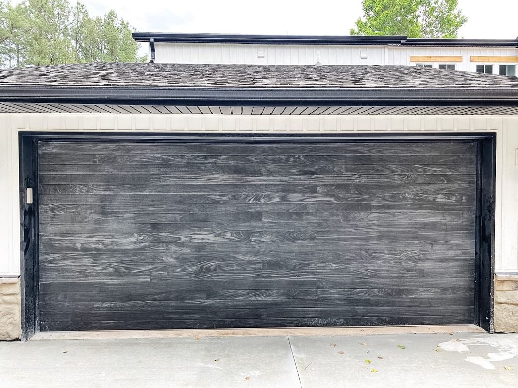 A black garage door is sitting in front of a white house.