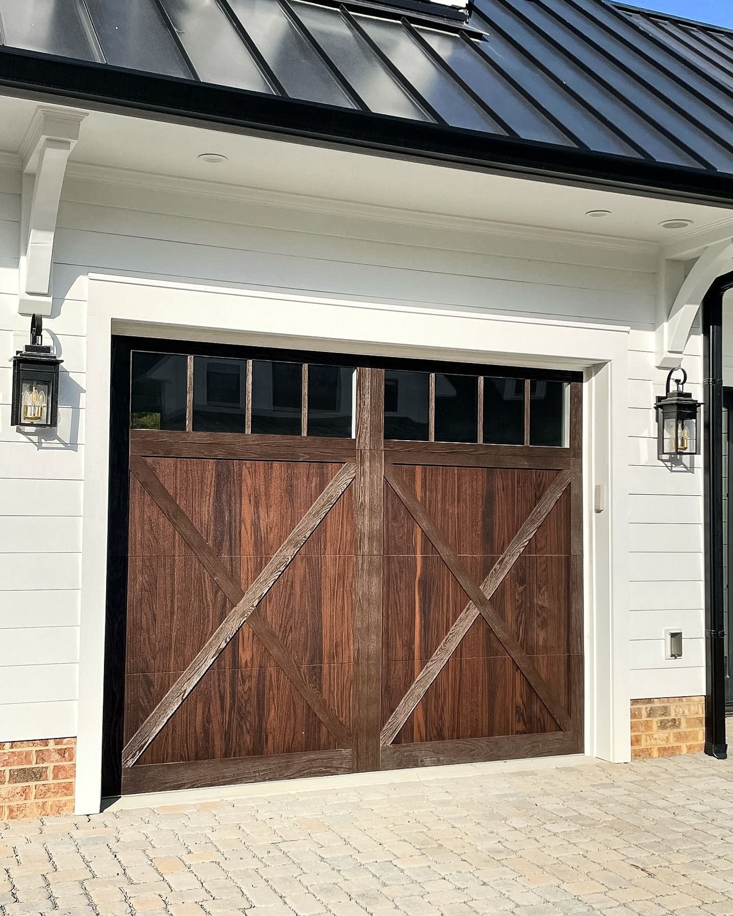 A wooden garage door is on the side of a white house.