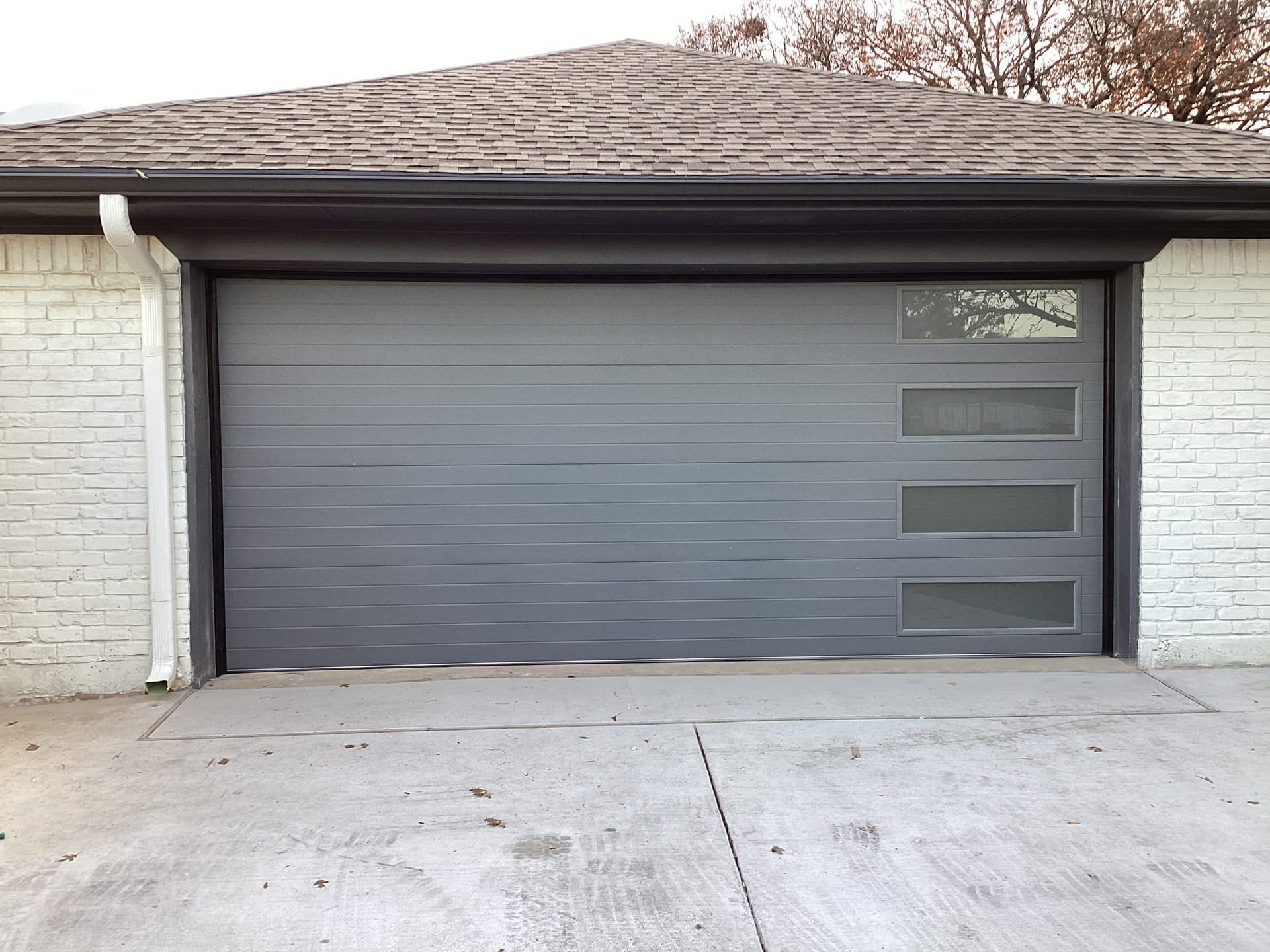 A gray garage door is sitting in front of a white brick house.