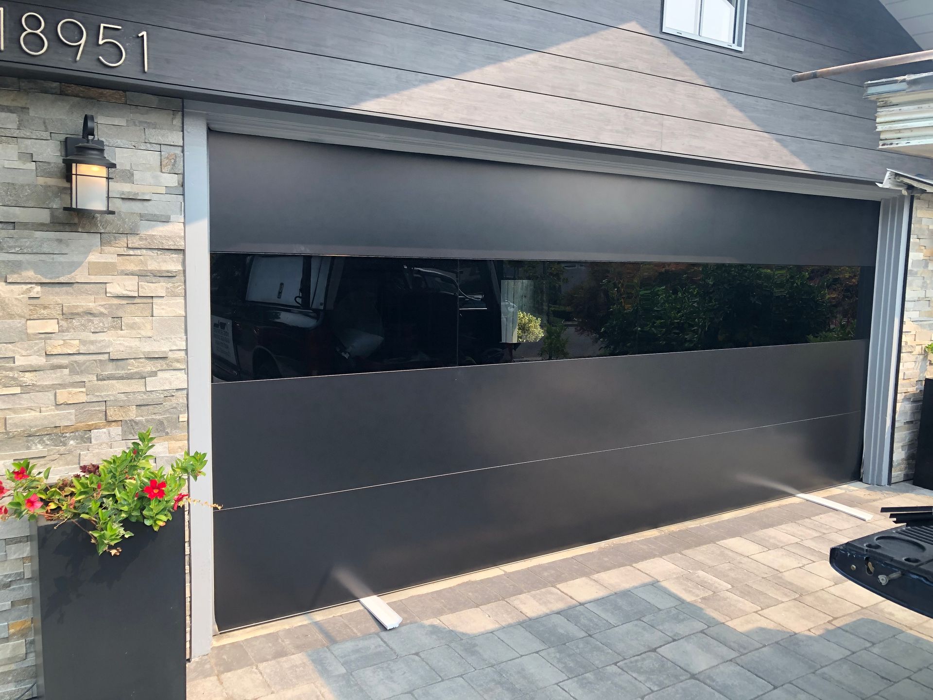 A black garage door with a large window and a brick wall.