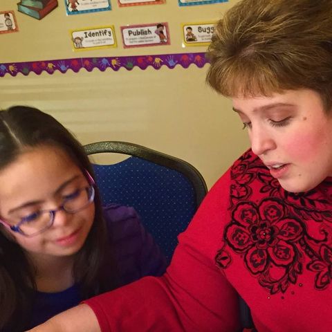 a woman in a red sweater is helping a boy with a piece of paper