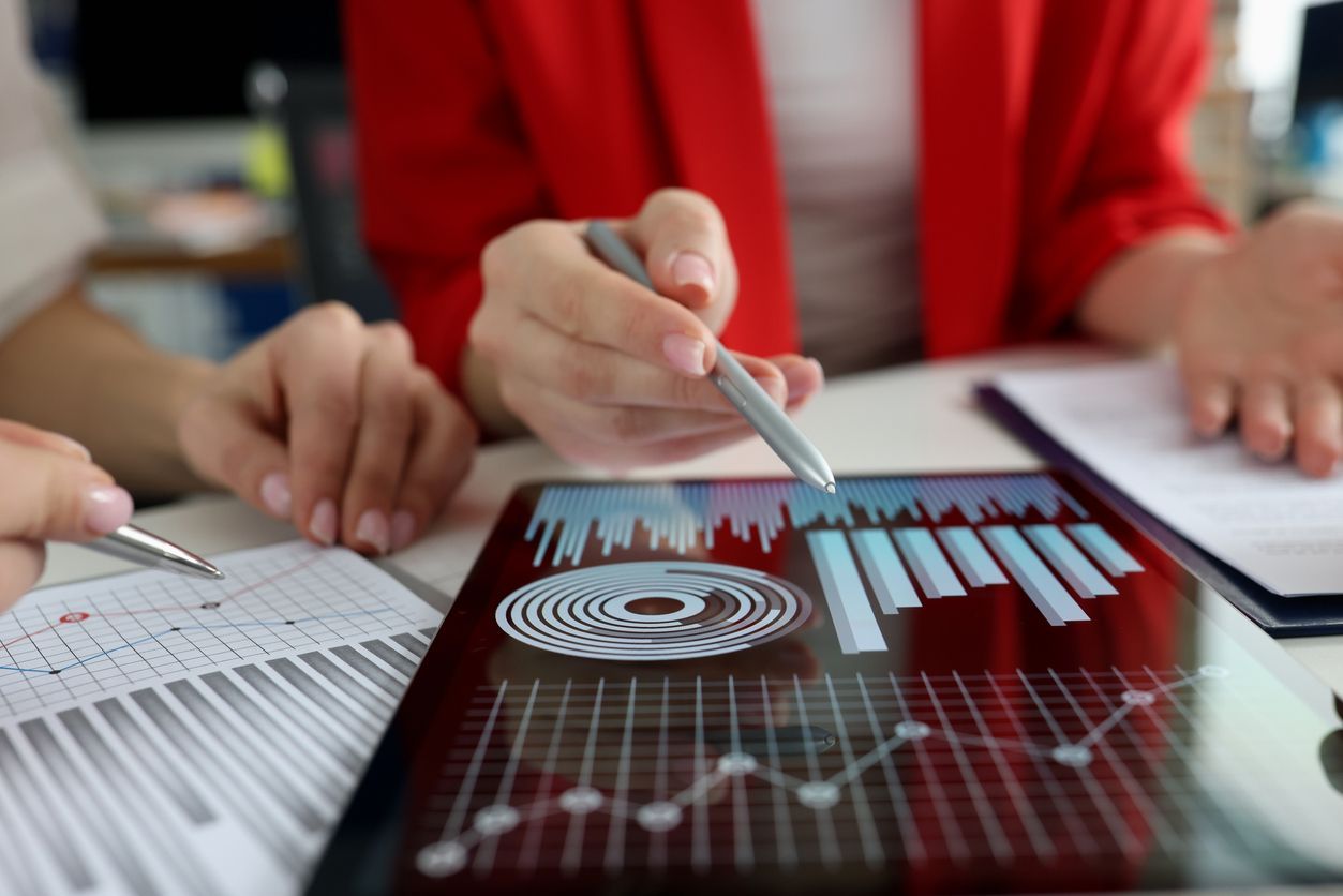 Personas señalando una tableta que muestra gráficos de datos en un entorno de oficina.