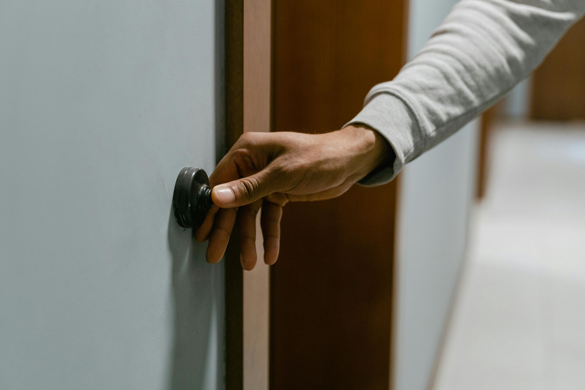 Una mano agarra el pomo negro de una puerta azul claro y la abre. Se ve un pasillo al fondo.